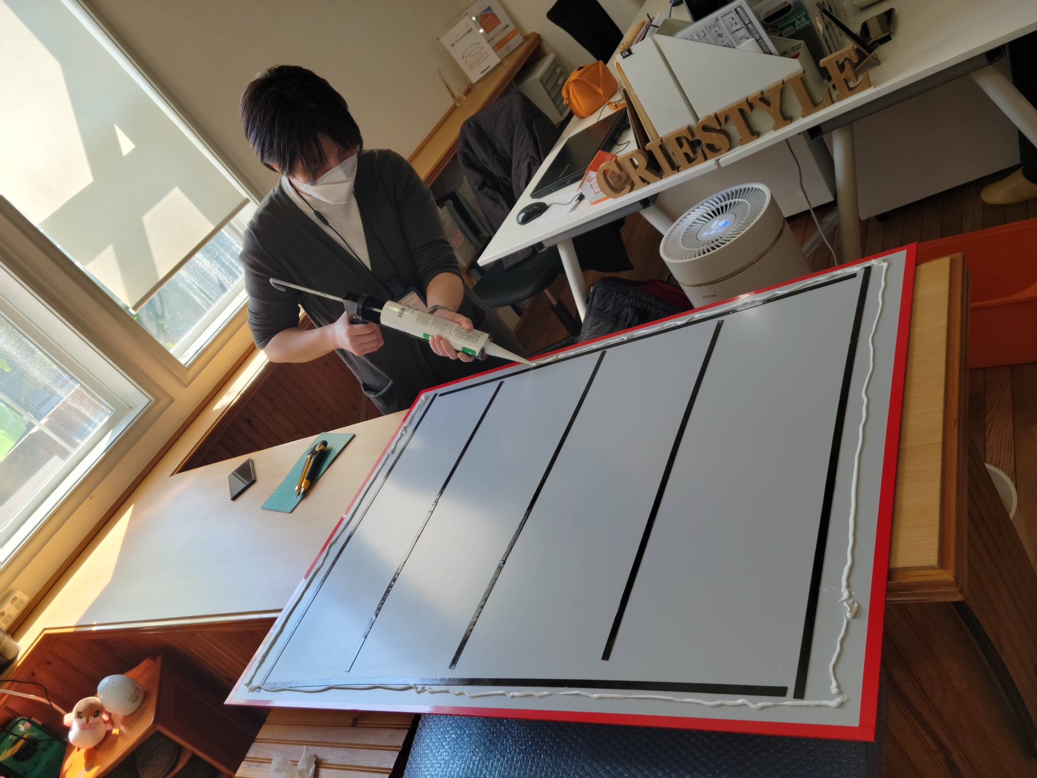 写真：奥田がコークガンを使って看板の裏面に接着剤を塗布する様子